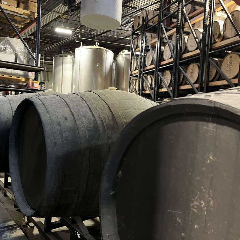 Large wooden barrels in a brewery with metal tanks and racks in the background.