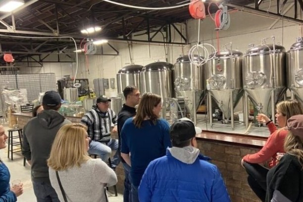 Group of people on a brewery tour, standing by large stainless steel tanks.