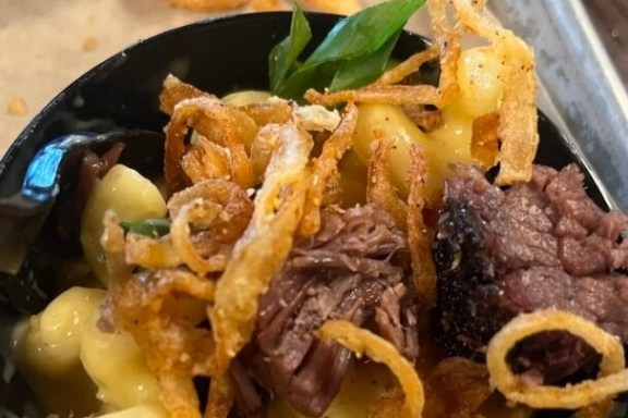 Bowl of pasta with beef, crispy onions, and herbs.
