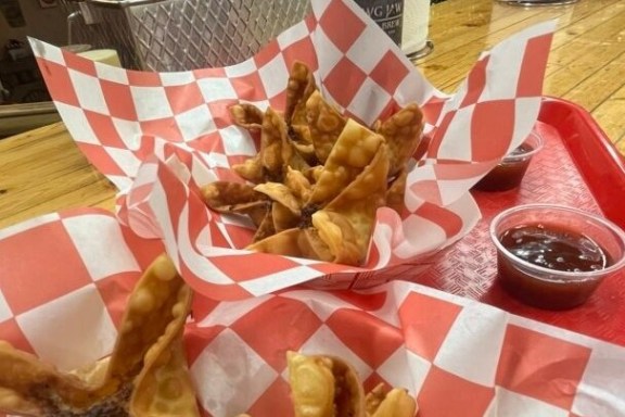 Crispy wontons in checkered paper with dipping sauces on a red tray.