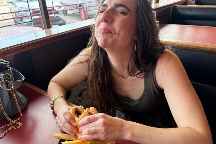 Woman smiling while eating a burger and fries at a diner table.