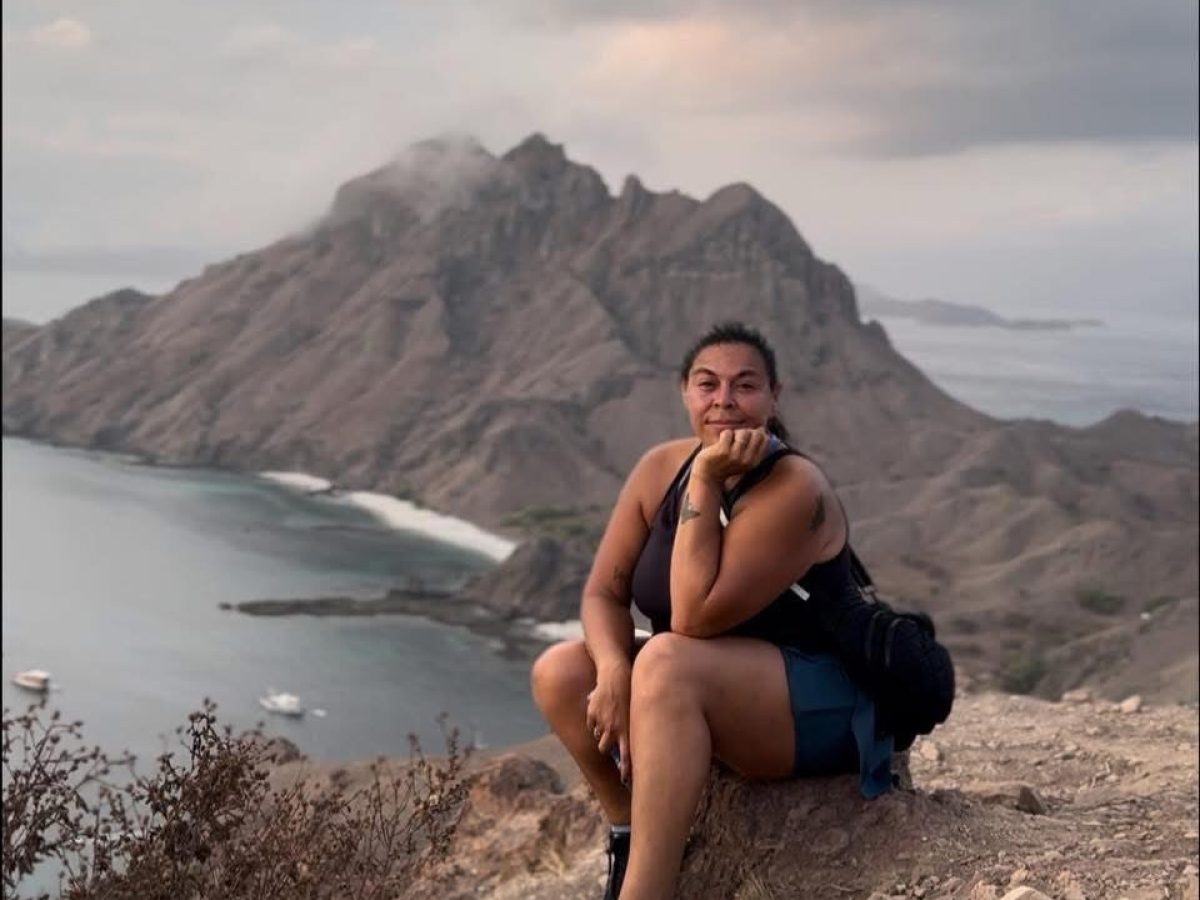 Person sitting on a rocky hill with a scenic view of mountains and sea in the background.