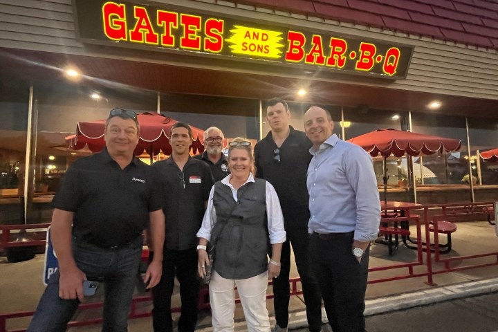 Group of six people smiling outside a restaurant with a Gates Bar-B-Q sign.
