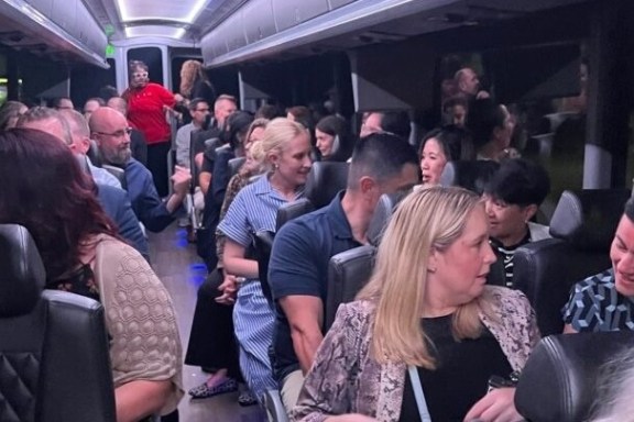 A group of people sitting and talking inside a well-lit bus with cushioned seats.